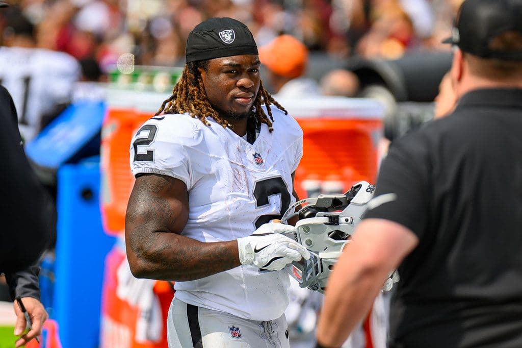 Ashton Jeanty in a white Las Vegas Raiders number 2 uniform holds his helmet on the sideline during a 2025 game.