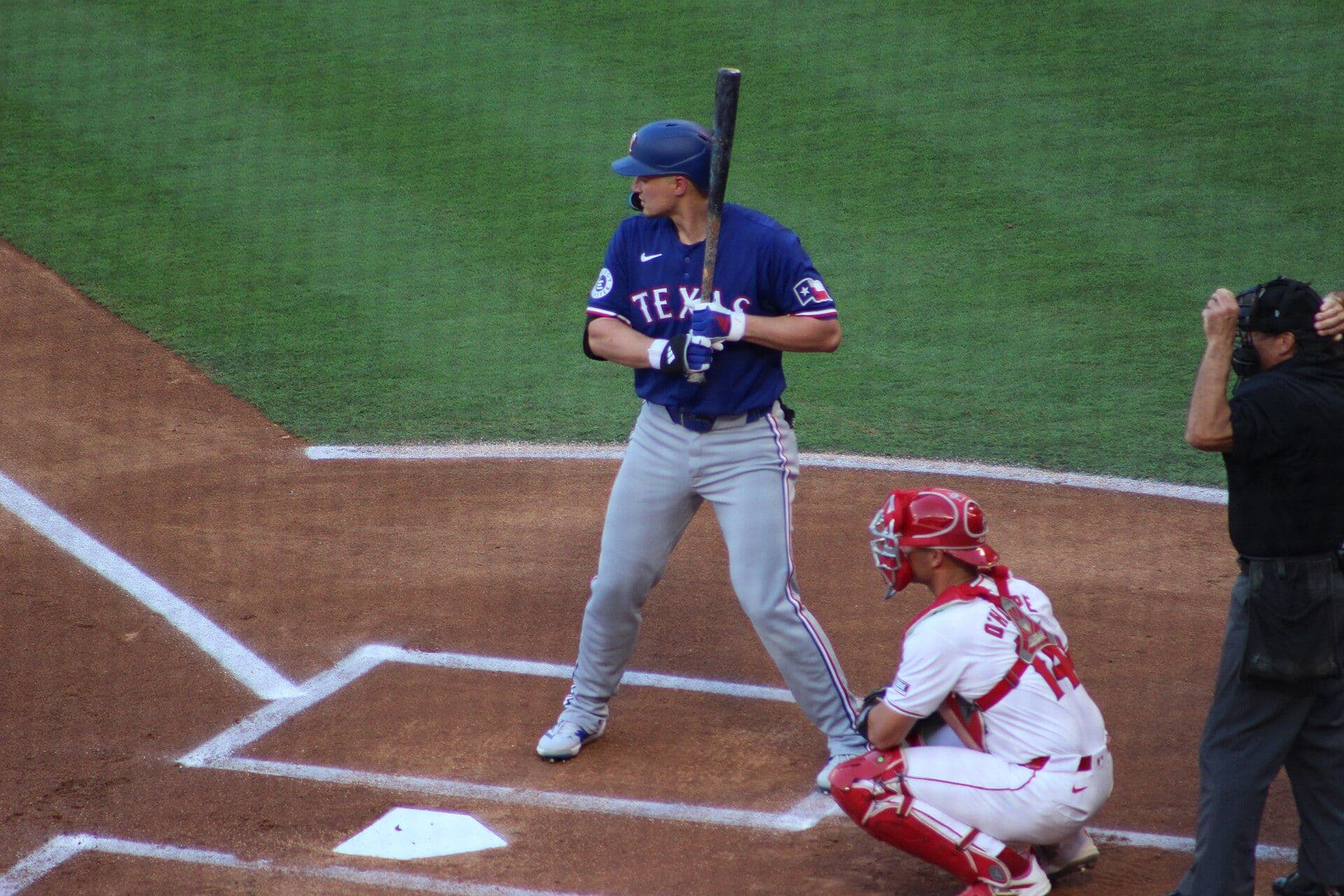 Corey Seager of the Texas Rangers stands in the batter's box in a blue Texas jersey over gray road pants, bat raised, waiting on a pitch.